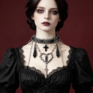 May include: A black choker necklace featuring a central silver-toned heart frame with thorns, a small black cross pendant, and dangling black teardrop charms. The piece is constructed with a black band, silver chains, and intricate metal detailing.