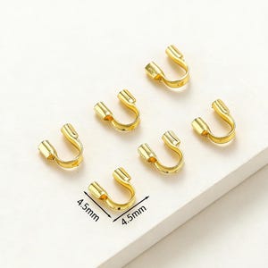 May include: Six gold-colored U-shaped jewelry findings, each measuring 4.5mm x 4.5mm. The findings have a rectangular base and a curved, open top, suitable for jewelry making. The findings are arranged on a white surface.
