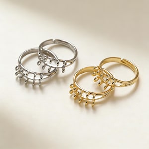 Puede incluir: Dos pares de anillos ajustables, uno plateado y otro dorado. Cada anillo presenta un diseño único con una serie de barras verticales y curvas. Los anillos se exhiben sobre una superficie beige claro.