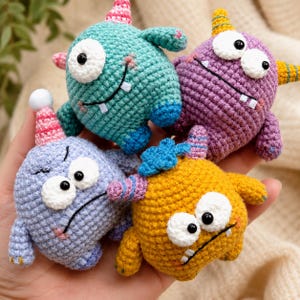 May include: Four small, round, crocheted monster toys in teal, purple, light blue, and yellow. Each creature features large white eyes with black pupils, small arms, and unique colourful horns or spikes on their heads, with stitched facial expressions.