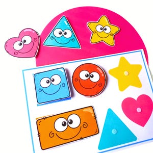 May include: A set of colorful educational shape cutouts featuring cartoon faces with large eyes and smiles. The collection includes a pink heart, blue triangle, yellow star, blue square, orange circle, and orange rectangle, arranged on a white board.