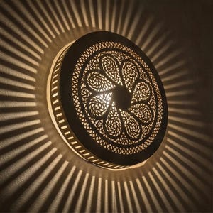 Puede incluir: Una taza de cerámica blanca con un asa negra y el texto "But First, Coffee" en negrita negra. La taza se encuentra sobre un fondo borroso, sugiriendo un ambiente acogedor.