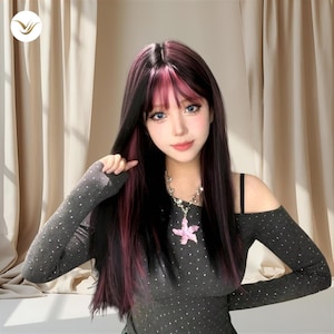 May include: A long black wig with pink highlights and bangs. The person is wearing a gray long-sleeve shirt with small, shiny embellishments and a silver necklace with a pink flower pendant. The background is a neutral beige.