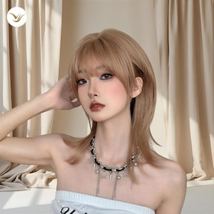 May include: A woman with light brown hair and bangs, wearing a black and silver necklace with star and teardrop charms. She is wearing a white strapless top. The background is a beige curtain.