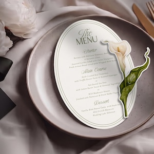 May include: An oval-shaped menu card with dark green text and a decorative border, featuring a printed white calla lily illustration with a green leaf. The text includes sections for Starter, Main Course, and Dessert, with the name Emily on the leaf.