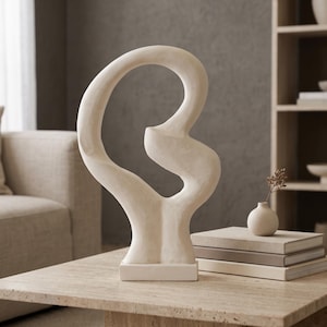 May include: A cream-colored abstract sculpture with a smooth, curved, and open-loop design mounted on a rectangular base. The sculpture features a continuous, flowing form that creates a large central void, finished in a matte, off-white texture.