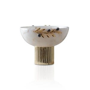 May include: A decorative bowl with a white marble finish, featuring a gold-colored base and olive branch accents. The bowl has a rounded shape and is supported by a fluted, gold-toned pedestal. The olive branch design includes black olive details.
