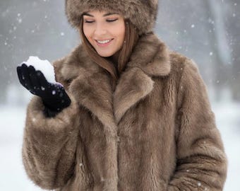 May include: A brown faux fur coat with a wide collar and long sleeves, paired with a matching brown faux fur hat. The coat features a thick, textured pile and a structured silhouette, providing full coverage for the upper body in cold weather.