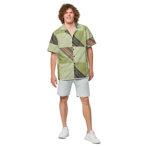 May include: A short-sleeved button-down shirt featuring a patchwork design of olive green, light green, and diagonal striped panels in brown, black, and white, paired with light gray shorts and white athletic sneakers.