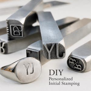 May include: A collection of metal initial stamps and a silver signet ring. The ring is engraved with the initials "YJ". The image also includes the text "DIY Personalized Initial Stamping".
