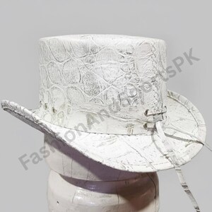May include: White top hat with a textured, crocodile-like pattern. The hat features a wide brim and a tall crown. It has eyelets and a tie detail on the side. The hat is made of a stiff material.