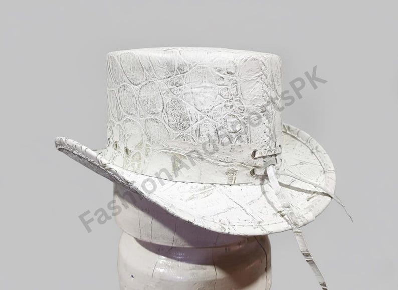 May include: White top hat with a textured, crocodile-like pattern. The hat features a wide brim and a tall crown. It has eyelets and a tie detail on the side. The hat is made of a stiff material.