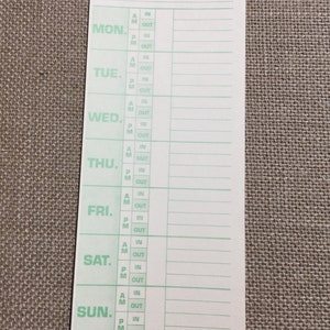 May include: A white time card with green text and lines for recording daily work hours. The days of the week are listed: Monday, Tuesday, Wednesday, Thursday, Friday, Saturday, and Sunday. The card has spaces for recording AM and PM in and out times.