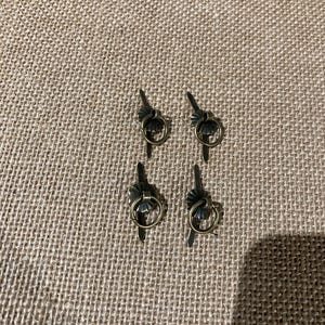 May include: Four antique brass drawer pulls with ring handles. Each pull features a decorative leaf design and a small ring for easy gripping. The pulls are arranged on a textured, neutral-toned surface.