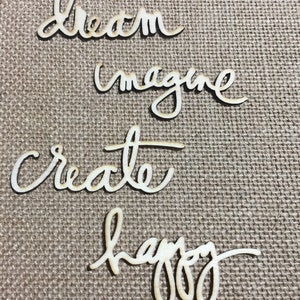 May include: Four wooden cutout words on a burlap background. The words are "dream", "imagine", "create", and "happy".