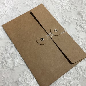 May include: A rectangular brown kraft paper envelope featuring a flap closure secured by two circular paper discs with silver metal eyelets and white string wrapped in a figure-eight pattern to keep the contents inside the envelope secure.