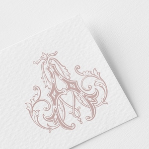 May include: A dusty rose coloured letter A rendered in a decorative calligraphic font with ornate flourishes and scrollwork details. The letter is printed on a white textured paper surface with a visible grain and a subtle diagonal orientation.