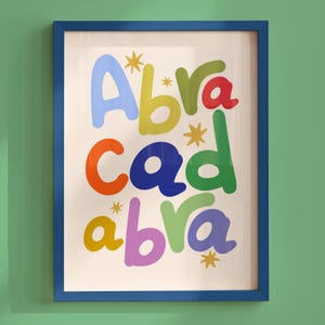 以下が含まれることがあります： カラフルで丸みを帯びたバブルスタイルの文字で「Abracadabra」と書かれた額入りウォールアートプリント。文字は3行に配置され、明るいクリーム色の背景に小さな黄色い星のアイコンが文字の間に散りばめられています。