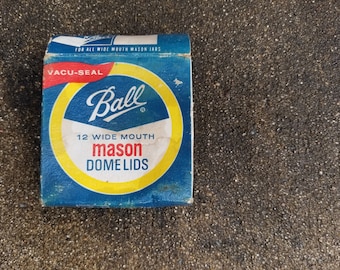 May include: A blue box of Ball brand mason jar dome lids. The box has a yellow circle with the Ball logo and the words "12 Wide Mouth Mason Dome Lids". The box also has the words "Vacu-Seal" and "For All Wide Mouth Mason Jars".