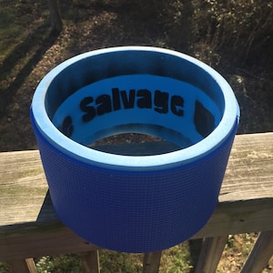 以下が含まれることがあります： 黒い文字で「Salvage」という文字が入った青い円筒形の物体。物体はテクスチャ加工された外側と、より明るい青色の内側を持っています。物体は木製の表面に置かれています。