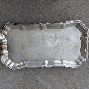 Peut inclure: Un plateau de service rectangulaire argenté avec des poignées décoratives. Le plateau a un bord festonné et une surface légèrement texturée. Les poignées sont incurvées et présentent des détails ornés. Le plateau est conçu pour servir des aliments ou des boissons.