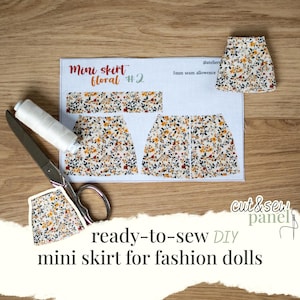May include: A ready-to-sew DIY mini skirt pattern for fashion dolls. The pattern includes pieces for a floral mini skirt, with a spool of white thread and scissors. The text "Mini skirt floral #2" is visible on the pattern.
