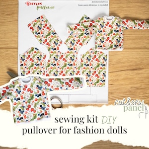 Puede incluir: Un kit de costura DIY para muñecas de moda con un diseño de jersey con estampado de bayas. El kit incluye piezas de tela recortadas y un jersey terminado del tamaño de una muñeca. Las palabras "Berries pullover" y "sewing kit DIY" son visibles.