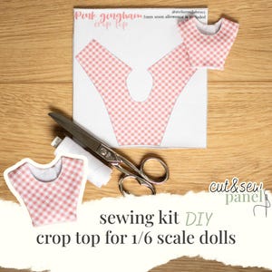 Könnte beinhalten: Ein DIY-Nähset für ein Crop-Top für Puppen im Maßstab 1:6. Das Set enthält ein rosa Vichy-Stoffmuster, eine Schere, Faden und den Text "Pink gingham crop top". Die Wörter "cut & sew panel" und "DIY" sind ebenfalls sichtbar.