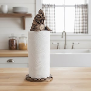 May include: A kitchen paper towel holder with a bronze-coloured rooster head. The holder sits on a roll of white paper towels and a wooden base, adding a rustic touch to the kitchen decor.