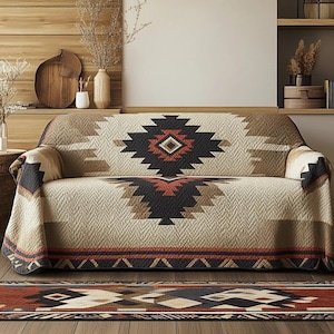 May include: A beige sofa with a geometric patterned cover in shades of black, brown, and rust. The cover features a central diamond design and a border with a repeating triangle pattern. A matching rug is visible in the foreground.