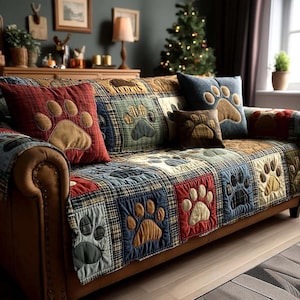 Può includere: Un divano in pelle marrone con una trapunta patchwork e cuscini con impronte di zampe. La trapunta presenta quadrati di tessuto a quadri in vari colori, ciascuno con un'impronta di zampa. I cuscini sono rossi, blu e marroni.
