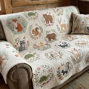 May include: A cream sofa cover and cushion set with embroidered woodland creatures in hexagonal patterns. The cover displays a fox, bear, deer, raccoon, squirrel, owl, skunk, and turtles. The cushion features owls and other forest animals.