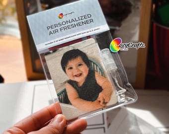 May include: A personalised air freshener featuring a baby's photo. The packaging is clear plastic, displaying the text "PERSONALIZED AIR FRESHENER" and the brand "cozyCrafts". Includes a 5 ml water-based scent refill, lasting up to 3 weeks.