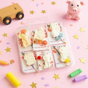 May include: A clear plastic package containing six DIY craft kits with vehicle-shaped plaster figures, paintbrushes, and paint. The kits are arranged on a pink surface with star-shaped confetti, a wooden toy truck, a pink pig figurine, and colorful markers.