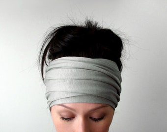 May include: A wide, light gray headband made of soft, stretchy fabric. The material features a series of horizontal, overlapping folds that wrap around the head, creating a layered, ruched appearance across the entire width of the accessory.