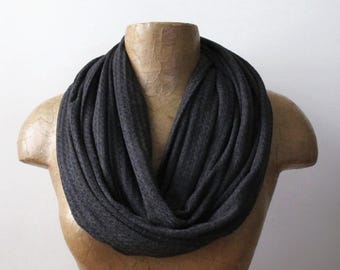 May include: A dark charcoal gray infinity scarf with a soft, heathered texture. The scarf is draped in multiple circular loops, creating a voluminous and layered appearance around the neck area, showcasing a consistent knit fabric throughout.