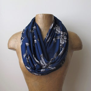 May include: A navy blue infinity scarf with a white floral pattern. The scarf is made of a soft, stretchy fabric and is perfect for adding a touch of style to any outfit.