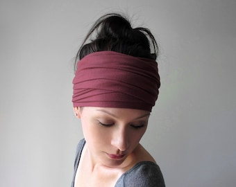 May include: A wide, dark rose-colored fabric headband featuring a gathered, ruched design that wraps around the head. The accessory is made of a soft, stretchy material with multiple horizontal folds creating a textured, layered appearance across the surface.