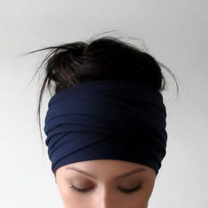 May include: A navy blue headband is wrapped around the head of a person with dark hair. The headband is made of a soft fabric and is wide, covering the forehead and ears. The person's eyes are closed.