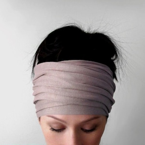 Peut inclure: Un bandeau de couleur taupe clair enveloppe le front. Le tissu est doux et semble être fait d'une matière extensible. Le bandeau est porté sur des cheveux foncés, les yeux de la personne étant fermés.