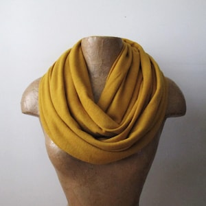 May include: A mustard yellow infinity scarf made of soft fabric. The scarf is folded and draped around a mannequin's neck.