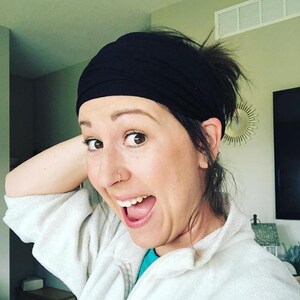 May include: A black headband worn on the head. The headband is made of a soft, stretchy material. The person is wearing a white jacket and a blue shirt.