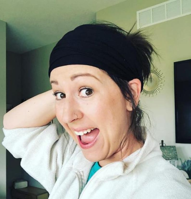 May include: A black headband worn on the head. The headband is made of a soft, stretchy material. The person is wearing a white jacket and a blue shirt.