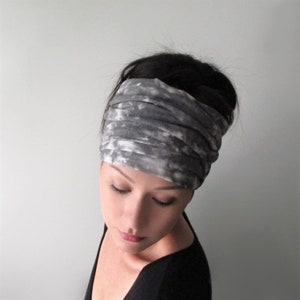 May include: A gray and white tie-dye headband worn on a person's head. The headband is made of a soft, stretchy fabric and is perfect for adding a touch of style to any outfit.