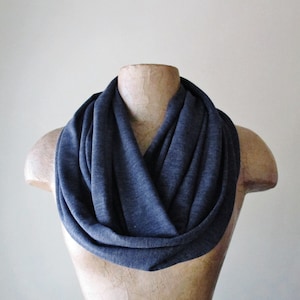 May include: A dark blue infinity scarf made of a soft, stretchy fabric. The scarf is folded and draped around a mannequin's neck.