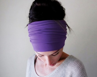 May include: A solid purple fabric headband featuring a wide, ruched design that wraps around the head. The headband is made of a smooth, stretchy material and is positioned across the forehead, providing a simple and functional hair accessory.
