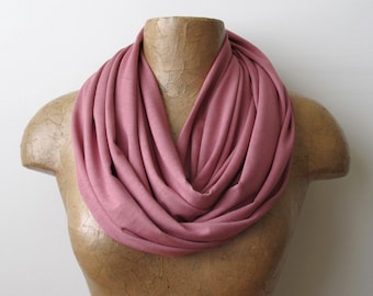 May include: A soft, pink infinity scarf made of jersey knit fabric. The scarf is draped around a mannequin's neck.