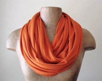 May include: A bright orange infinity scarf made of soft fabric. The scarf is draped around a mannequin's neck.