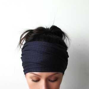 May include: A wide, dark navy blue headband made of a textured, ribbed fabric. The accessory features a layered, wrapped design that sits horizontally across the forehead, covering the hairline and extending around the head in a continuous band.