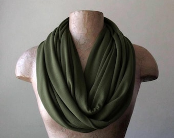 May include: Olive green infinity scarf draped on a mannequin. The scarf is made of a soft, flowing fabric and is wrapped multiple times around the neck, creating a layered effect. The color is a muted, earthy green.